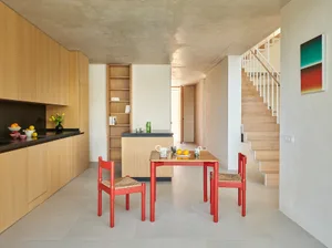 Modern kitchen and dining area with wooden cabinets, red chairs, and a cozy atmosphere, featuring a main dining table and a smaller table nearby