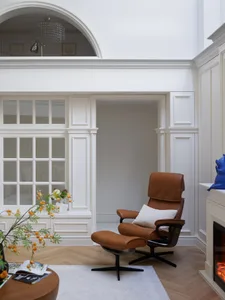 A well-lit room with a brown leather chair in front of a window, accompanied by a smaller chair in the background, creating a comfortable and inviting atmosphere