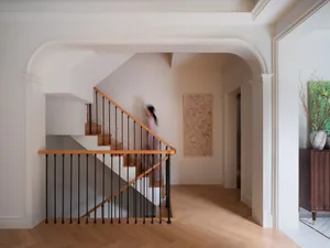A person stands at the bottom of a staircase with wooden steps and black metal railings, against a white wall in a calm and inviting atmosphere