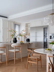 A well-designed kitchen and dining area with wooden floors, white cabinets, and a cozy atmosphere, featuring a potted plant and several chairs