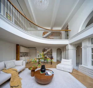 Open living space with white walls, wooden floors, and a staircase, featuring two couches, a coffee table, and a potted plant