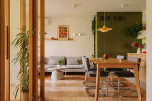 Open plan living and dining area with a wooden dining table, potted plant, and comfortable couch, surrounded by chairs and vases