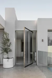 Open modern living area with a glass door leading to a patio, a white bed in a bedroom, a couch, and neutral tones