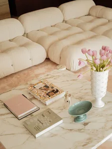 Cozy modern living space with white couches, chairs, and a coffee table, featuring books, a vase with flowers, and clean lines