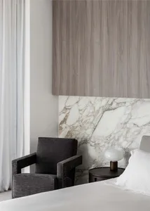 A bedroom with a marble wall, two chairs, and a couch, featuring a clock on the wall and an elegant atmosphere