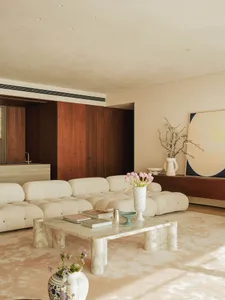 A cozy living area with a white couch, carpeted floor, chairs, a dining table, vases, and a potted plant