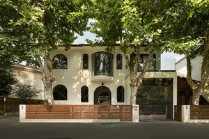 A modern house with a brown wooden fence in front, surrounded by trees and featuring several windows on its facade