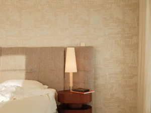 Cozy bedroom with a bed, nightstand, and patterned wallpaper, with a warm and inviting atmosphere