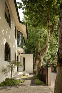 A modern house with a white exterior, surrounded by trees, featuring large windows, potted plants, and a bench, conveying a sense of comfort and relaxation