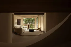 Cozy open living area with two couches, a chair, and a potted plant, surrounded by natural light and a large window overlooking a garden