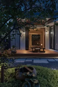 Serene Asian-style house with a wooden deck and patio area, featuring greenery, trees, and grass
