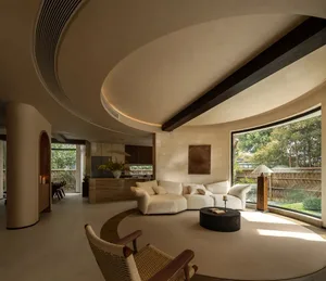 Open modern living area with a circular design, white walls, and a large window allowing natural light, featuring two couches and potted plants