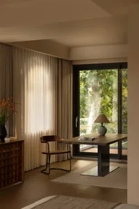 A cozy dining space with a wooden table and chairs, surrounded by large windows and a potted plant, filled with natural light