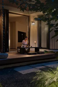 A well-lit living area with a woman sitting at a table, surrounded by a couch, chair, and TV, creating a cozy atmosphere