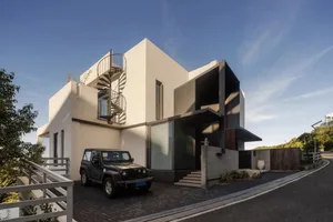 A modern house with a white exterior and black accents, featuring a two-story staircase and two cars parked in front
