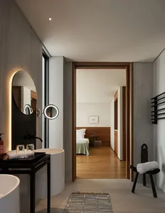 Well-lit bedroom with wooden floors and walls, featuring a large mirror, two beds, and a chair, creating a cozy and inviting atmosphere