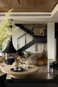 Cozy living space with a staircase, two chairs, a dining table, vases, and cups, surrounded by comfortable furniture and inviting decor