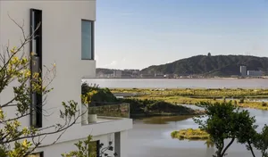 A white house situated on a hillside overlooking a large body of water, with several windows and a picturesque view from the balcony