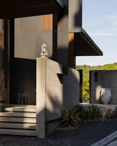 A modern house with a black exterior, featuring a stone patio, concrete staircase, and decorative vases and a chair in a well-manicured outdoor setting