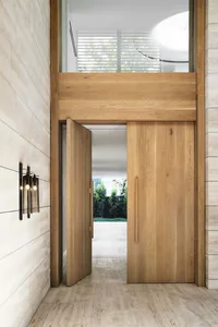 A spacious living area with a wooden doorway, large window, potted plants, and a chair, filled with natural light