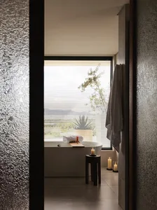 A modern bathroom with a bathtub next to a window, candles, and a potted plant, creating a bright and inviting atmosphere