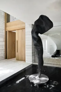 A black and white sculpture of a leg on a pedestal in a room with a large window, two chairs, and a bright atmosphere