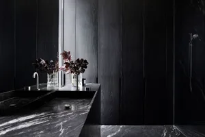 Dark and moody bathroom with a black wall, wooden countertop, and two vases on the sink area