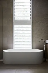 A bathroom with a white bathtub next to a window, surrounded by blinds, creating a calm and relaxing atmosphere