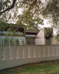 A modern house with a white exterior, surrounded by trees, featuring a large window and a well-maintained, well-lit atmosphere