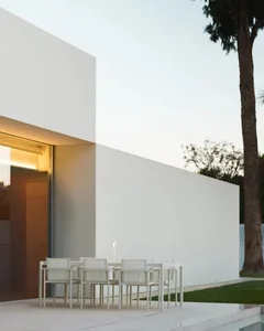 A modern outdoor patio with a dining table and white chairs, surrounded by a white building and a potted plant, creating a comfortable and inviting atmosphere