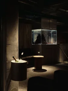 Cozy living room with a large aquarium, a couch, and a dining table, featuring wood and glass materials in a dimly lit space