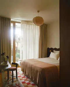 Cozy bedroom with a bed, chair, and dining table, featuring wood and fabric materials, warm colors, and natural lighting