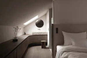 Dimly lit bedroom with a bed, sink, and mirror, featuring wood materials and neutral colors