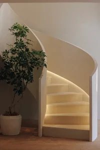 A staircase with a white railing and a potted plant, set in a calm and inviting hallway with natural light from a window