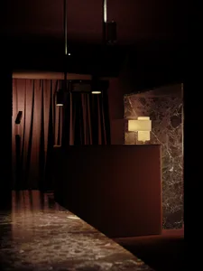 Dimly lit hotel lobby with a marble countertop, a brown table, and a lamp, set against a neutral background