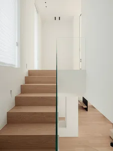 A modern staircase with wooden steps and a glass railing in a bright and airy white house