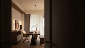 A well-lit modern living room with a dining table, chairs, and a vase, surrounded by wood furniture and filled with natural light