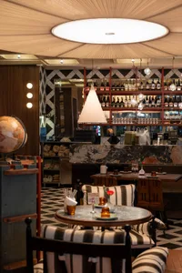 A modern restaurant interior with a well-stocked wine bar, dining table, and potted plants, creating a cozy atmosphere for wine and dining