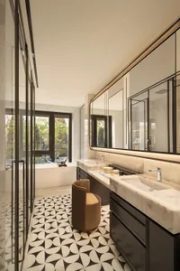 Well-lit bathroom with a sink, mirror, and chair, featuring marble and wood materials