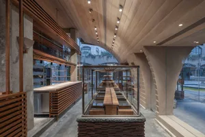 A modern restaurant interior with a long wooden table, chairs, and a counter with sink and refrigerator, featuring warm and inviting lighting