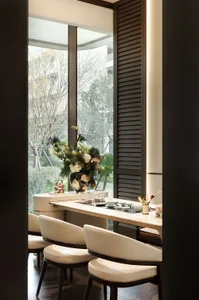 A dining room with a wooden table and chairs, a potted plant, and natural light from a window