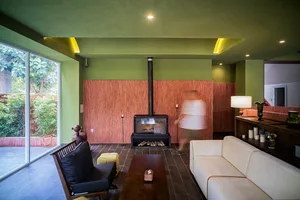 Cozy living room with a fireplace, green walls, and a dining table, surrounded by a couch and a chair