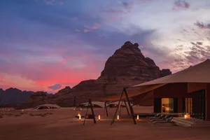 Desert landscape with a large rock formation in the background, set at sunset with warm colors and natural elements