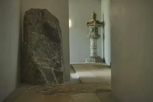 A dimly lit hallway with a stone floor, a stone pillar, and a statue, creating a solemn and quiet atmosphere