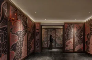 A calm and inviting hallway with Asian-style artwork on the walls, a person walking towards the camera, and a handbag visible in the scene