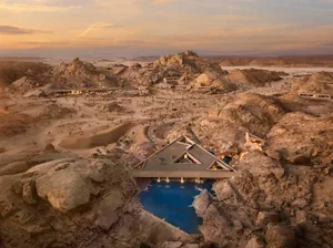 A modern resort building with a central pool surrounded by a rocky landscape, featuring a mix of natural and man-made elements