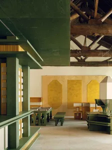 Cozy modern living-dining space with a green color scheme, wooden floor, and vaulted ceiling, featuring a dining table and chairs, and scattered books