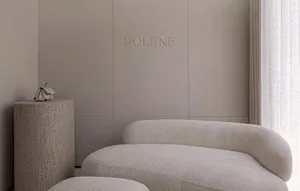 A modern living room with a white couch and a chair, soft lighting, and a logo on the wall