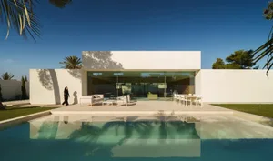 A modern house with a white exterior, glass door, and a pool area with patio furniture and a dining table, surrounded by a bright and inviting atmosphere
