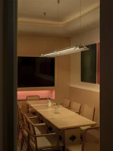 暖融融的餐廳用餐空間，擁有一長的木桌、椅子和一盆植物，周圍充滿自然光線和牆上的電視